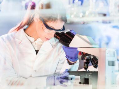a female doctor in a lab coat looking through a microscope
