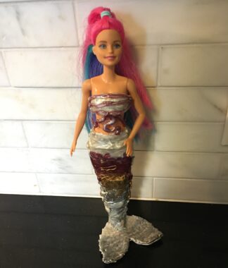 A closeup of a Barbie doll with long pink and blue hair and wearing a homemade mermaid tail.