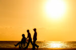 Two people walking with a person in a wheelchair at sunset on the beach