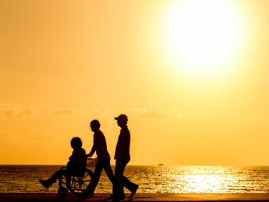 Two people walking with a person in a wheelchair at sunset on the beach