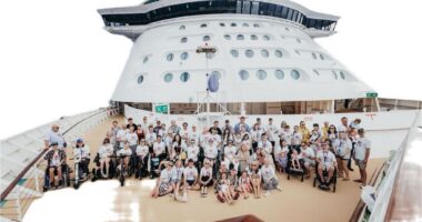 A large group of people, some of them in wheelchairs, gather on the top deck of a cruise ship.