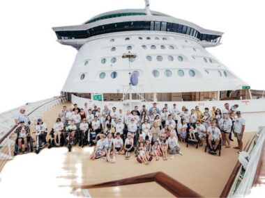 A large group of people, some of them in wheelchairs, gather on the top deck of a cruise ship.