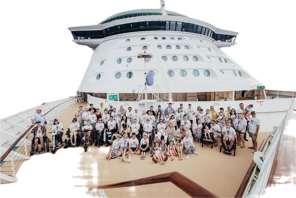 A large group of people, some of them in wheelchairs, gather on the top deck of a cruise ship.